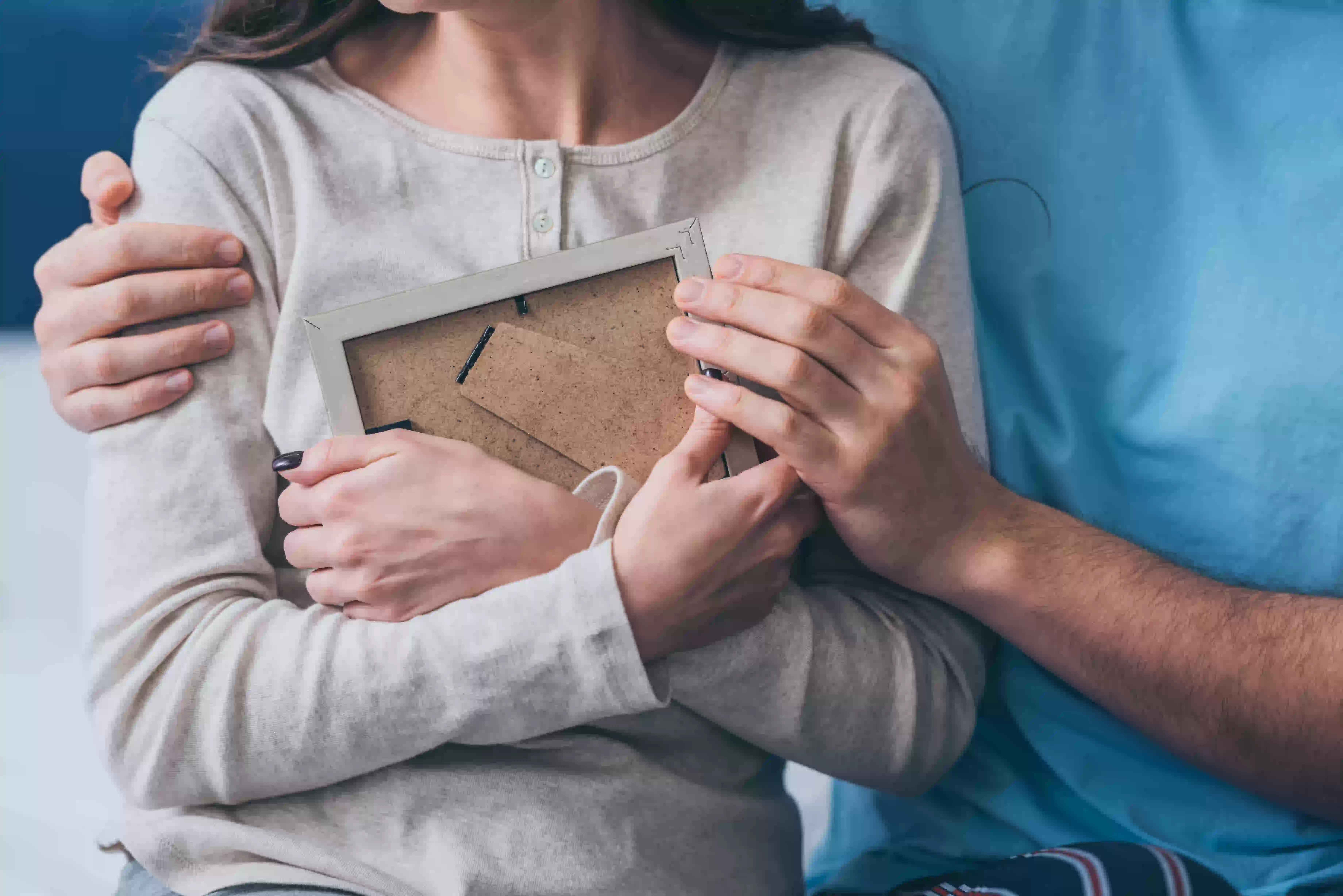 woman hugging a photo frame while man hugging her