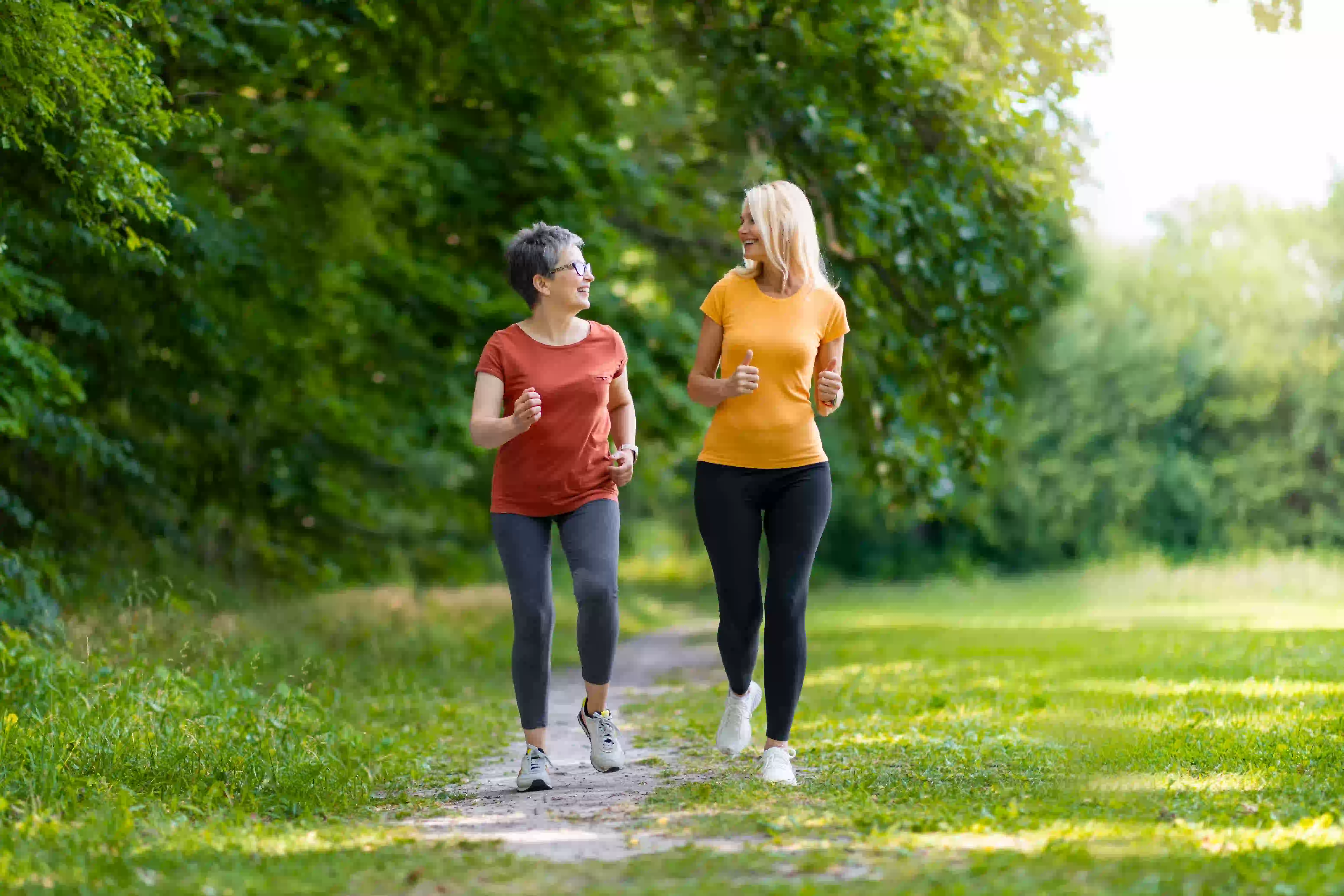 two women jogging at the park with a lot of trees around