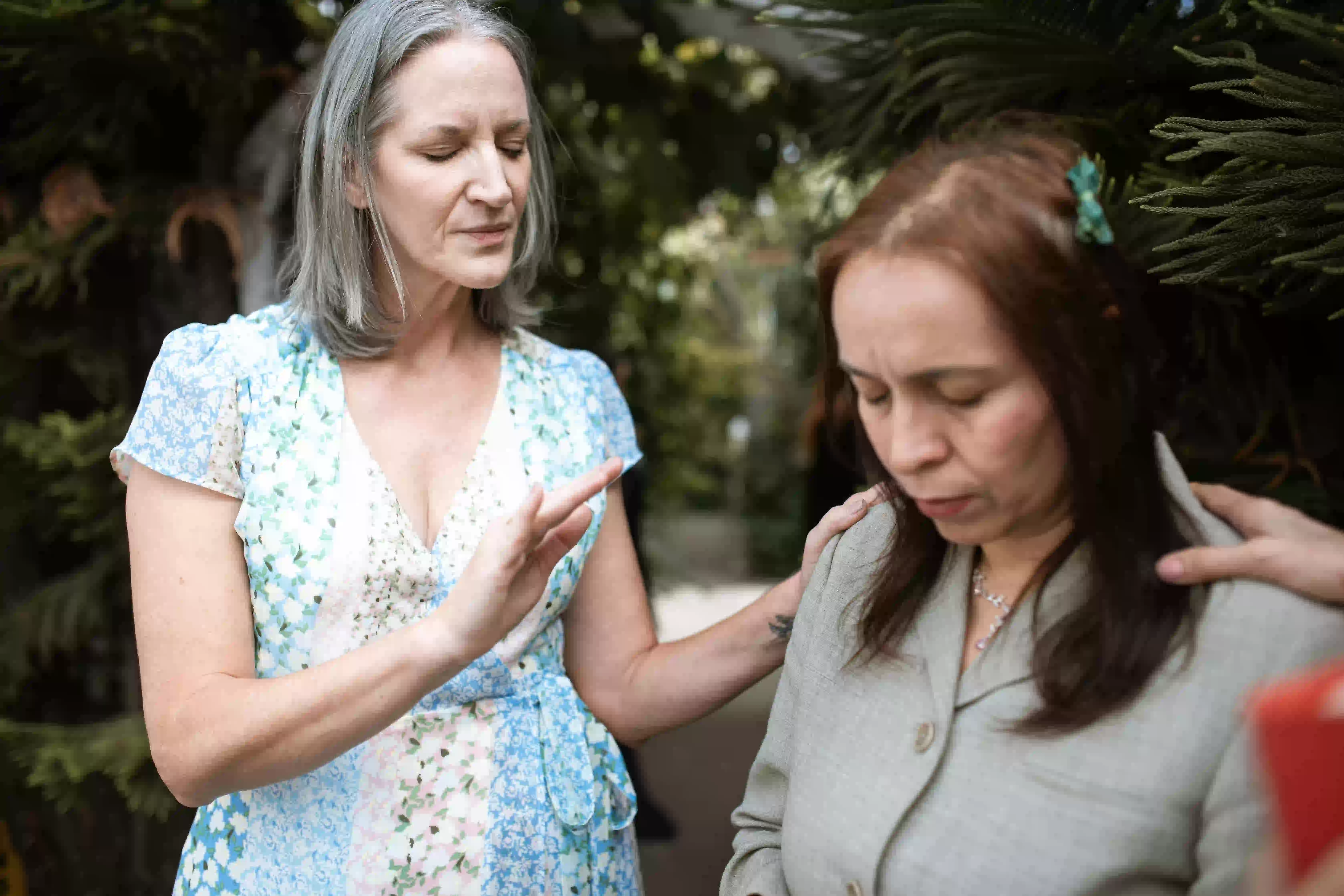 woman laying hands on another woman closing eyes and praying