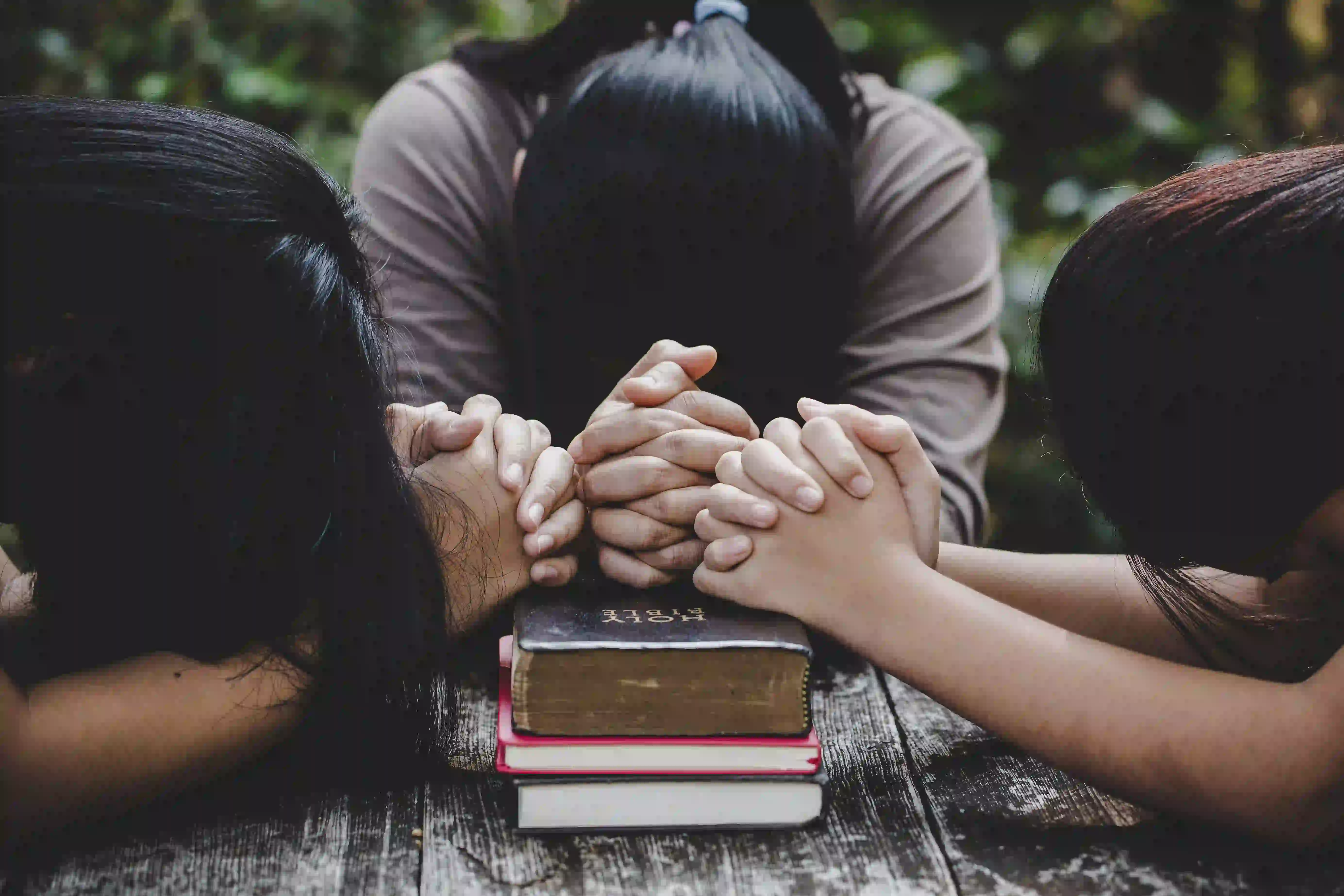 women bowing in prayer hands above the Bible 